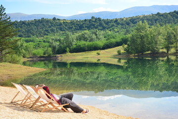 Frau entspannt im Liegestuhl am Idyllischen See Perućko Jezero bei Sinj, Vrlika in Kroatien mit Bäumen und Berge im Hintergrund