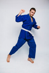 Young man in a blue kimono on a white background. The guy is a beginner in martial arts.