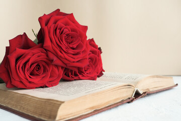 three red roses on an open old book on a table on a beige background..copy space.