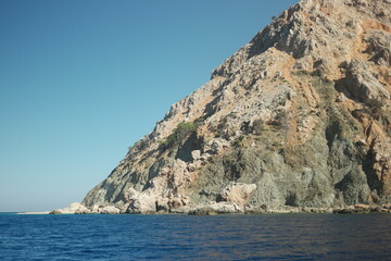 Dark blue sea and big stone formation in the background. Cliff over sea surface under blue sky.