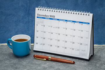 December 2021 - spiral desktop calendar against abstract paper landscape with a cup of coffee, time and business concept