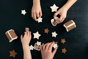 Children are playing with Christmas gingerbread cookies. Top view on black background
