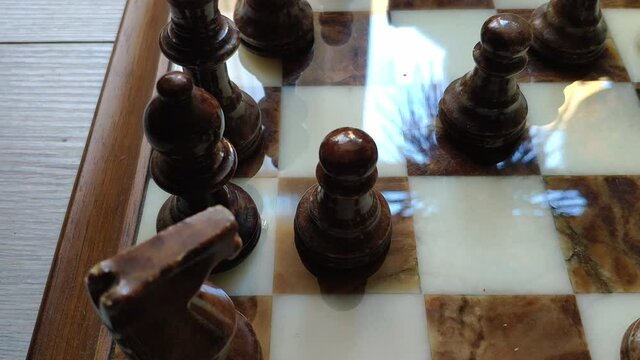 Marble chess game. It's bright and the board and pieces shine with reflections. A pawn is moved forward one square and then moved back again.