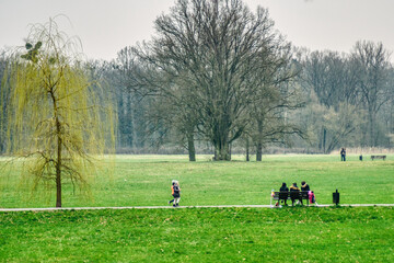 dzieci z dorosłymi odpoczywają w parku, wiosenne spacery na świeżym powietrzu, krajobraz przedwiośnia w parku