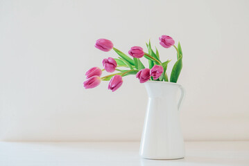 Beautiful mono bouquet of purple tulips in full bloom in white vase on white background. Copy space for text. Spring still life.