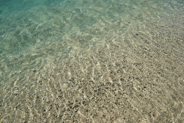 Pebbles in transparent sea water. Texture of transparent crystal clear sea water and pebbles. Marine background.