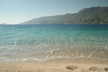 Sandy beach with crystal clear sea water. Green mountains and blue sky in the background. Beautiful marine landscape.
