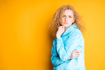 Sad woman leans on one hand while standing against bright orange background