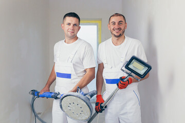 Plasterer smoothes the wall surface with a wall grinder. Two master builders grind a white plaster...