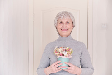 A portrait of a smiling elderly Caucasian woman with a bouquet of dried flowers.