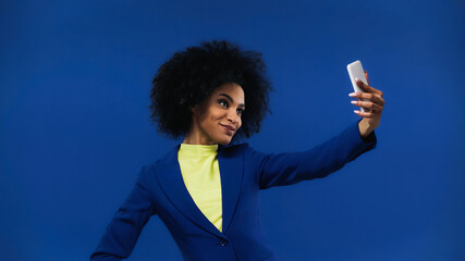 Smiling african american woman taking selfie isolated on blue