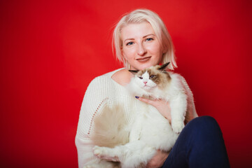 Young woman hugs a ragdoll cat on a red background. Love to the animals.