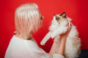 Obraz premium Young woman hugs a ragdoll cat on a red background. Love to the animals.