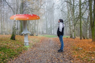 A young man stands in the middle of an autumn landscape and stares at a giant two meter high...