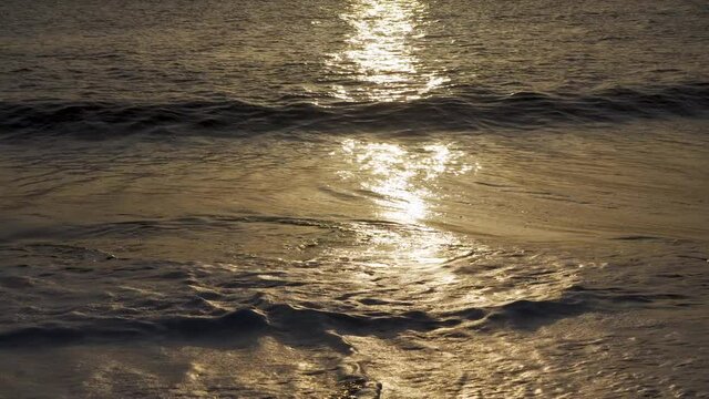 Sun lit waves crashing on a sandy beach during sunrise.