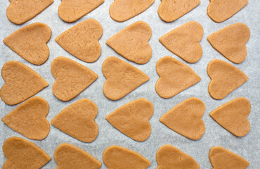 Raw homemade cookies in the shape of heart on a baking sheet. 