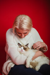 Young woman hugs a ragdoll cat on a red background. Love to the animals.