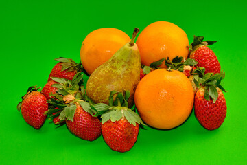 Strawberries, pears and oranges on a green background.