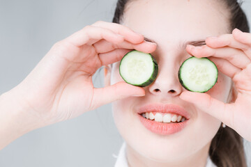 Happy woman holds cucumber slices in front of her eyes. Cucumber mask to preserve youthful skin