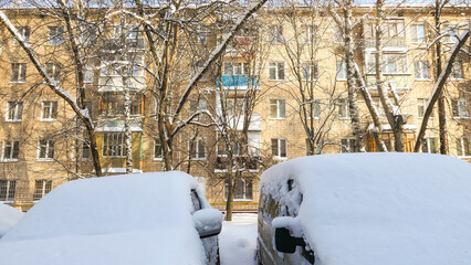 Snow covered yard with residential house wall and naked tree branches in sunny winter in Moscow