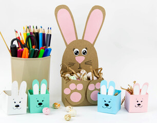 Crafts with children for Easter from colored paper. Boxes bunnies for sweets in the form of eggs. Flat lay.