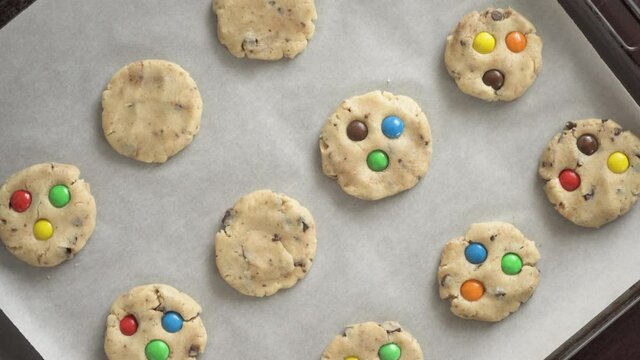 A woman decorates a raw cookie on a baking sheet with colorful M&Ms candies