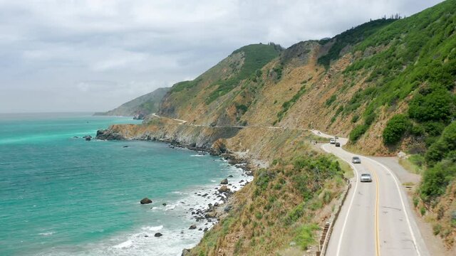 Aerial close up of Pacific Coast Highway, Northern California USA. Cinematic nature landscape with coastal winding road with beautiful blue green Pacific ocean waters. Rocky cliffs with green hills 4K