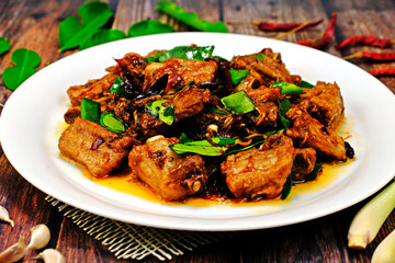 Stir fired pork rips with chilli, lemongrass and kaffir lime leaves surrounded by key ingredients on wooden table. Authentic Thai food.