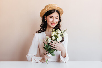 Ecstatic korean woman smiling while posing with flowers. Blithesome curly asian girl holding white eustomas.