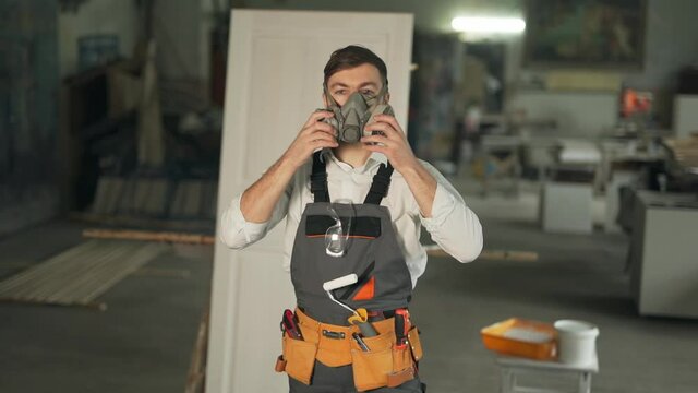 Pleasant man in the work uniform of a painter wears respirators and goggles