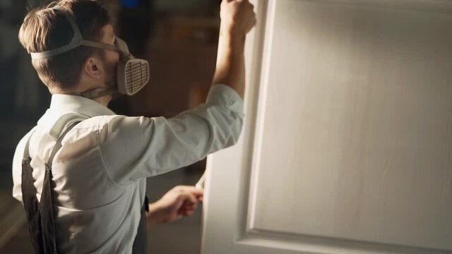 Painter paints a wooden door with a paint roller in white