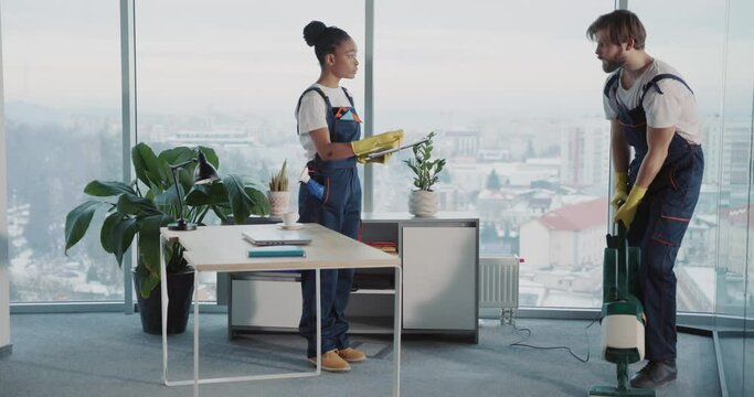 Young caucasian cleaner worker tidying corporate office with vacuum cleaner. Young angry chief cleaner woman complaining and shouting on lazy janitor. Conflict concept.