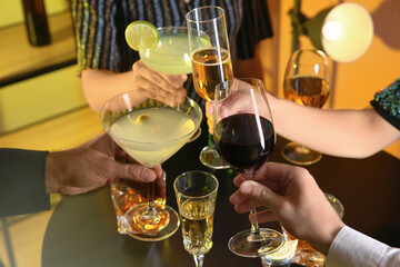 People with different alcohol drinks clinking glasses indoors, closeup