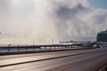 Foggy winter day in a city. A road and frost fog over the river in Siberia. Copy space, stock photo