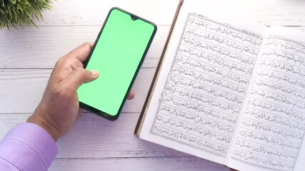 hand using smart phone and holy book Quran and rosary on table, 