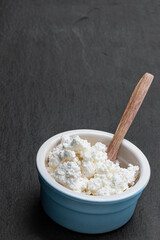 Cottage cheese in ceramic bowl on black stone background