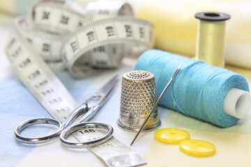 sewing accessories with blue and yellow threads, tape measure and scissors on fabric background
