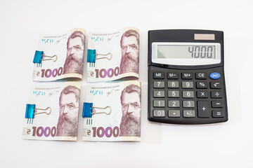calculator and 1000 hryvnia fastened by a clip on white.