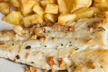 Close-up of garlic and spices on a hake fillet and french fries.