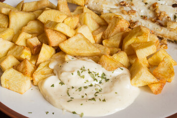 Close-up of aioli sauce with parsley accompanied by potatoes and fish on a plate. Homemade food.