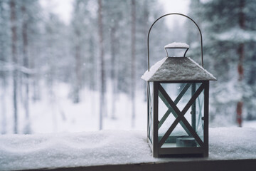 Lantern, flowers pot covered with the snow on a terrace on the snowy and frosty forest background. Selective focus.