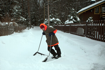 Young man shoveling snow from the walking path in winter.