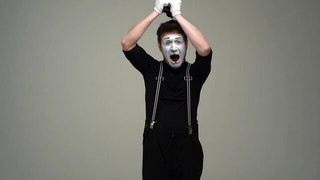 Portrait of suffering male mime hat off head, tearing hair and crying looking at camera. Talented actor wearing hat and gloves showing pantomime on white isolated background. Shooting in slow motion.