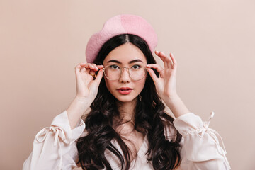 Portrait of asian girl touching glasses. Front view of stylish korean model in french beret.