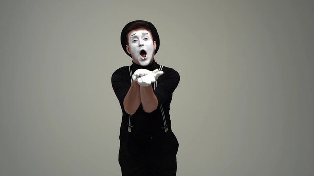 Portrait of happy male mime bowing in gratitude and applauding looking at camera. Talented actor wearing hat and gloves showing pantomime on white isolated background. Shooting in slow motion.