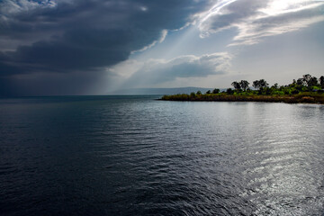 View of the Sea of Galilee or Kinneret Lake with rainy clouds and sun beams. Northern israel