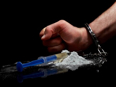 Handcuffed man and cocaine drug powder pile and injection syringe, arrested drug dealer