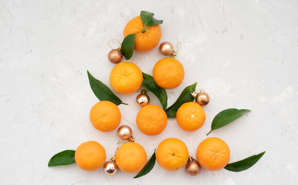 Christmas tree made of tangerines, the mood and taste of the new year, decorated with christmas golden little balls, mandarins on gray background. Fruits contain many vitamins good for healthy © vera