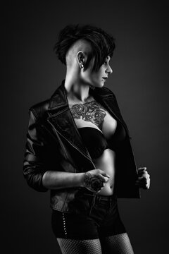 Attractive tattooed young woman, in profile, with a punk hairstyle, wearing a bra, leather jacket and fishnet stockings