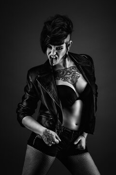 Pretty young tattooed woman, full face, with punk hairstyle, wearing bra, leather jacket, fishnet stockings, sticking out her tongue
